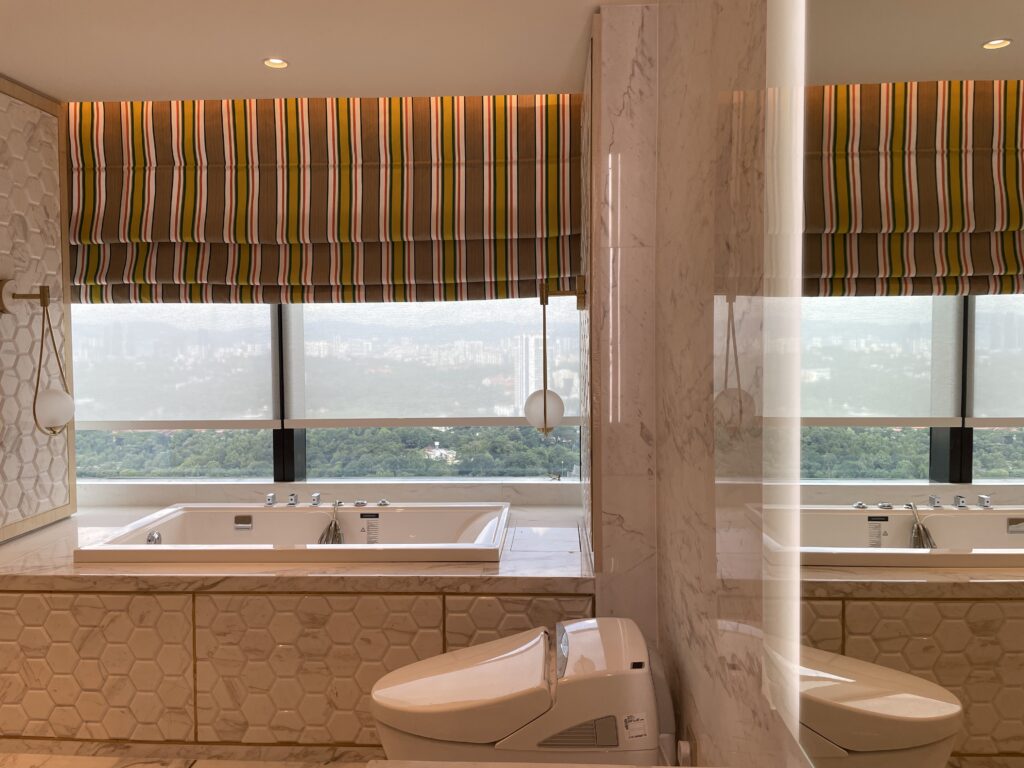 Roman blinds fitted above a luxury bathroom bathtub, adding soft privacy, warm colour, and a refined decorative window finish.
