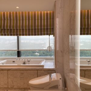 Roman blinds fitted above a luxury bathroom bathtub, adding soft privacy, warm colour, and a refined decorative window finish.