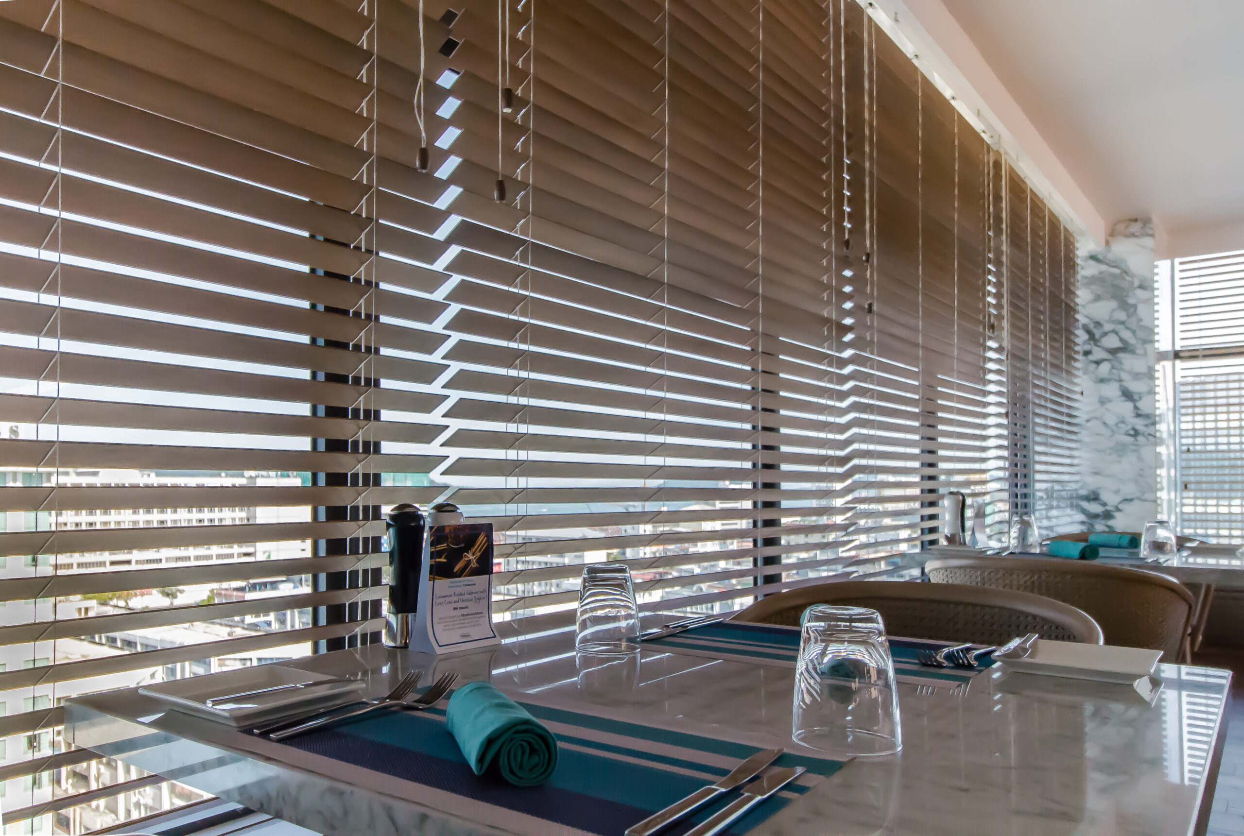Wooden venetian blinds installed in a bright dining area, offering refined privacy, adjustable daylight, and a polished interior finish.