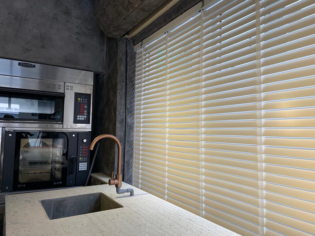 Wooden venetian blinds fitted beside a modern kitchen counter, balancing privacy, soft daylight, and a clean refined interior look.